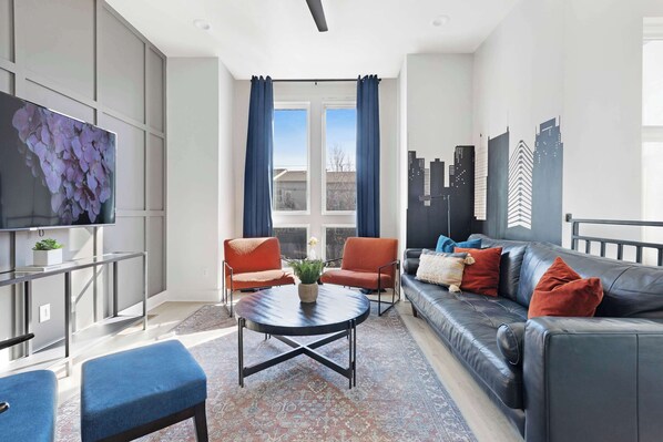 Stylish living room featuring a wall-mounted smart TV, cozy leather couch, sleek coffee table, and three elegant accent chairs for a comfortable and inviting space