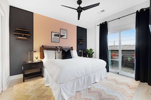 Spacious bedroom with a king bed, walk-in closet, and private balcony with two chairs. Features an en-suite bathroom with a sleek shower.