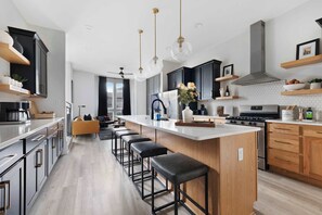 The spacious kitchen offers ample cabinet storage and counter space, an oversized island with five barstools, and clear sightlines into the living area.