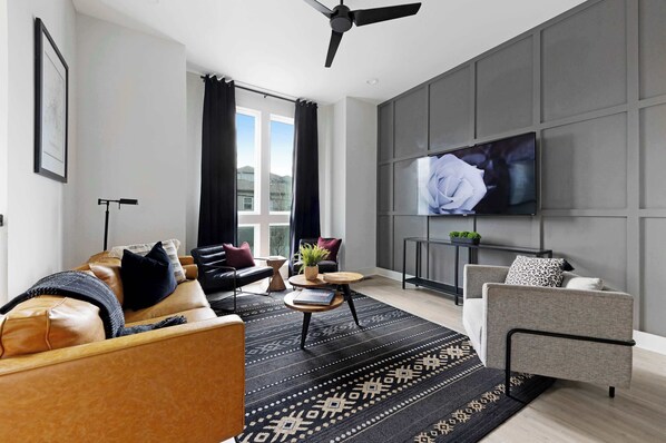 The cozy yet modern living space features a 65-inch, wall-mounted Roku television, perfect for streaming your favorite shows and movies.