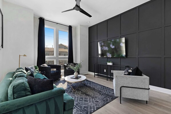Chic living room featuring a wall-mounted smart TV, a plush velvet couch, a stylish coffee table, and three accent chairs, offering a cozy yet elegant atmosphere