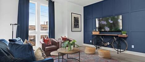 Inviting living room with a wall-mounted smart TV, a pull-out sofa bed, a stylish coffee table, and comfortable accent chairs, perfect for relaxing and entertaining.
