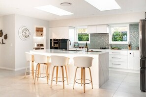This kitchen is designed with a beautiful grey backsplash that adds a modern, elegant touch to the space. The white cabinetry contrasts perfectly, and the lighting is well-placed and plentiful, ensuring the entire space feels inviting and well-lit.