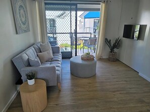 Cozy living room with a comfortable gray sofa, modern decor, and natural light. The space opens up to a balcony, perfect for relaxing or enjoying a quiet evening. The TV and stylish furnishings create an inviting atmosphere for unwinding.