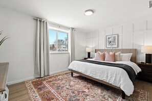 Retreat to this serene bedroom featuring a plush king bed, elegant board-and-batten accent wall, and abundant natural light—designed for restful nights and cozy mornings.