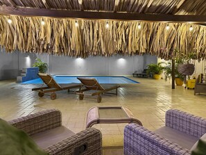 Indulge in luxury at Beach Walk 4, where cozy seating beneath a charming thatched roof overlooks a sparkling pool, creating an idyllic oasis for relaxation!