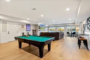 A bright and inviting recreation area with a pool table, comfortable seating, a bar area, and large windows showcasing scenic views.