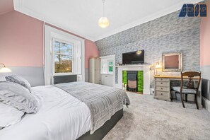 Sophisticated Relaxation: Enjoy the spacious master bedroom with linked single beds that form a super king, a decorative fireplace, a TV for entertainment, and a well-appointed dresser/desk and chair for all your needs