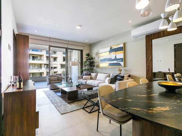 Enjoy the seamless flow of an open-concept living space designed for comfort and style. This inviting space features contemporary furnishings, a cozy sofa, and a large smart TV, perfect for relaxing or entertaining. The layout effortlessly connects the living area to the dining space and fully equipped kitchen, creating the ideal environment for gathering with family and friend...