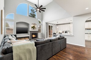 Spacious living area with stunning high ceilings, a warm fireplace, and an open flow into the kitchen—perfect for gatherings.