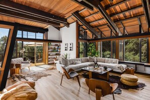 Mid-century modern meets nature! This stunning living space features exposed beams, floor-to-ceiling windows, and warm wood accents, blending style with serene outdoor views