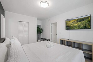Relax in this serene bedroom featuring a plush bed, modern TV, and minimalist decor for a peaceful retreat.