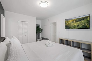Relax in this serene bedroom featuring a plush bed, modern TV, and minimalist decor for a peaceful retreat.