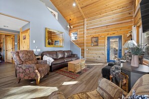 The cozy living room features large windows that fill the room with natural light, offering stunning views and a welcoming, open atmosphere.