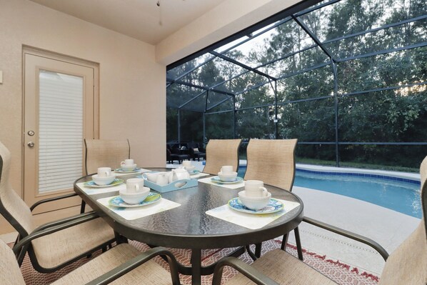 The outdoor dining features a dining table for six, flat screen TV, ceiling fan and pool views.