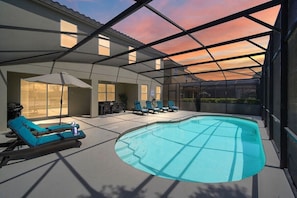 Beautiful sunny pool deck with a covered lanai and dining area, sun loungers, and a serene lake view.