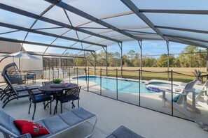 This screened-in outdoor area features a private pool, relaxing spa, safety fence for added peace of mind, multiple loungers, covered dining area with seating, and open views of the surrounding landscape