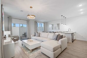 Open-concept design combines a cozy living area with a sleek, modern kitchen - Perfect for entertaining with extra seating, chic lighting, and a large sectional - Enjoy seamless indoor-outdoor flow through patio doors leading to a private retreat