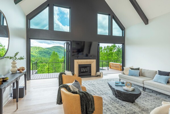 Stylish living room with floor-to-ceiling mountain views, an 85" Smart TV (streaming only), and deck access. Note: The fireplace is NOT usable.