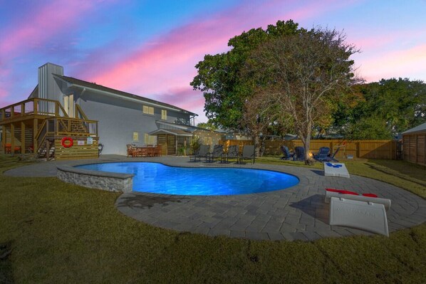 An evening view of the back of the house with the pool, softly lit for a peaceful and relaxing atmosphere under the stars.