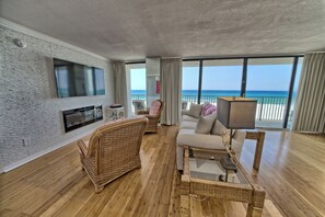 The living room offers comfortable seating, a large television, electric fireplace, and floor-to-ceiling gulf views.