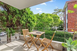 Start your day on the sunlit balcony with coffee at the table for two, surrounded by the calming view of lush greenery—a perfect setting to plan your beachside adventures.