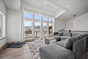 Experience the cozy living room, outfitted with plush seating, an expansive smart TV, and sliding patio doors that frame the breathtaking mountain vistas.