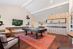 Primary open floor living space featuring a smart flat-screen TV, shuffleboard, pool table, and designer furnishings.