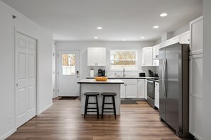 Large kitchen with island seating, stainless steel stove, dishwasher, and large refrigerator. Door to access backyard.
