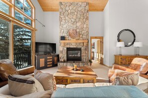 Living area with a gas fireplace, flat-screen TV, ample seating, and large windows with slope views.