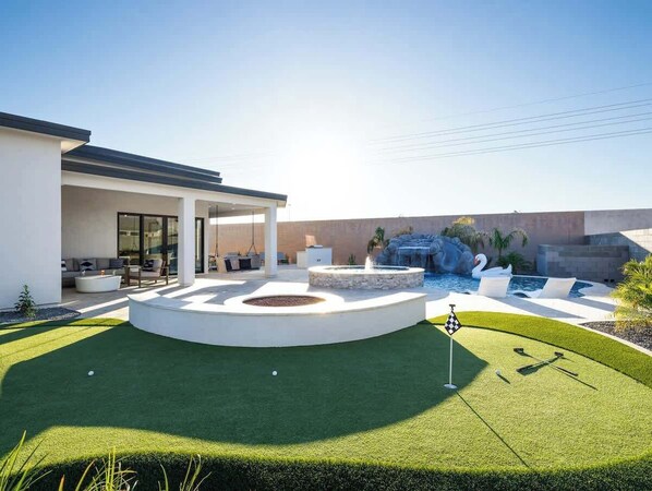 Backyard with large patio, firepit, putting green. Seating area for firepit and putting green.