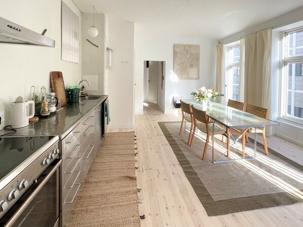 Large living -dining area with open kitchen in stainless steel, lots of sun