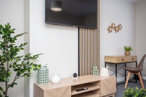 A sleek living room with a wooden TV stand, plants, and a desk area.