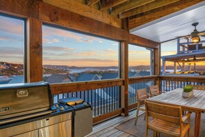 - Take in stunning lake views and golden hour skies from this inviting covered deck
- Fire up the grill & enjoy meals at the wooden dining table while watching the sun set
- Surrounded by wood beams, this space blends outdoor comfort & scenic charm