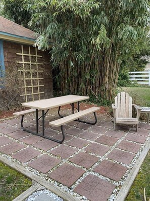 Serene backyard patio with a picnic table and Adirondack chair, perfect for outdoor dining or relaxing by the rose garden.