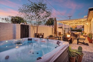 A cozy hot tub nestled in a beautifully designed lounge area, perfect for evening relaxation and conversation. The hot tub itself is inviting, with warm, bubbling water that seems to glow softly, creating a soothing ambiance.