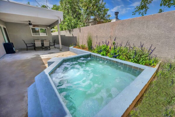 Unwind in the bubbling hot tub surrounded by vibrant flowers. Just steps away, a covered patio with a 6-seat dining table offers the perfect spot to dine or relax in the shade.