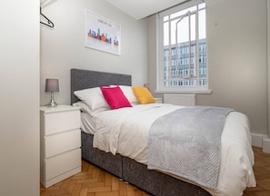 An elegant double bedroom with a plush bed for a restful night's sleep, along with a bedside table featuring a lampshade and a drawer for storage.