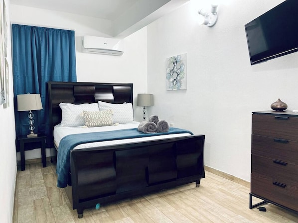 MAIN BEDROOM WITH QUEEN SIZE BED SMART TV AIRCONDITIONER LARGE W INDOW CURTAIN BED SIDE TABLE WITH LAMP  