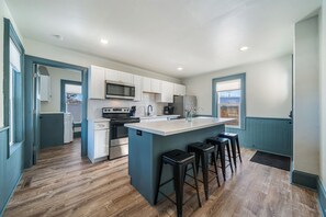Functional kitchen with ample counter space and a large island with seating for four. Equipped with essential appliances like a microwave, oven, fridge, and dishwasher. Stylish teal cabinets and white subway tile backsplash add charm.
