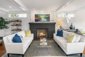 Relax in the sun-drenched living area, featuring a floor-to-ceiling fireplace and elegant coastal décor.