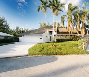 Admire the front view of our house with palm trees and a driveway spacious enough for six cars.