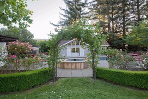 Stroll through this enchanting garden archway, surrounded by blooming roses and lush greenery, leading to a serene backyard oasis.