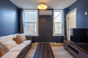 Bright and stylish living room with large windows, cozy seating, and a smart TV.