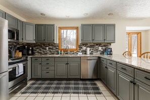 This modern kitchen features sleek gray cabinetry, stainless steel appliances like a refrigerator, oven, microwave, and dishwasher, and a spacious countertop with seating.
