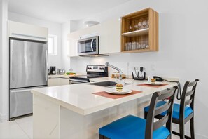 Well-equipped kitchen with a microwave, coffee maker, toaster, and large refrigerator with a sleek countertop and stylish bar stools.