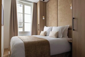 Une chambre parée d’un lit Queen size, d'une penderie, d'une TV et sa salle d'eau attenante équipée d'une douche et d'un lavabo.