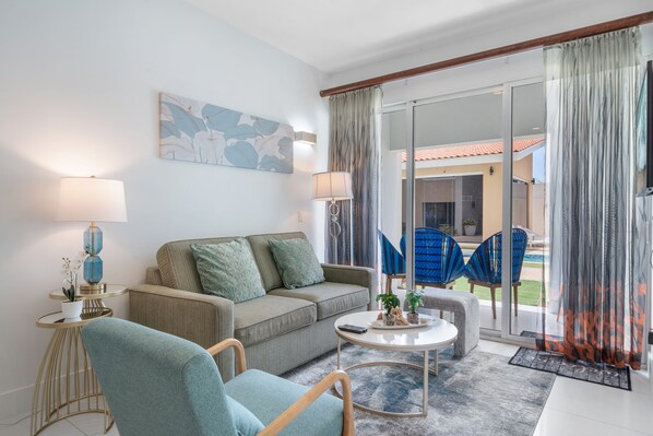 Stylish living area with a plush sofa & vibrant decor for a relaxing atmosphere - Large sliding glass doors fill the space with natural light & lead to outdoor patio - Perfect spot to unwind, watch TV or enjoy a morning coffee with a beautiful view