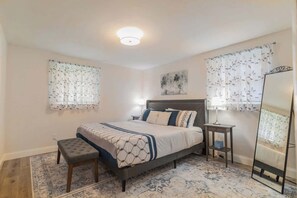 King bedroom with stylish side tables, warm lighting from bedside lamps, and a full-length mirror. Closet includes 2 luggage racks, laundry basket, and iron for added convenience.