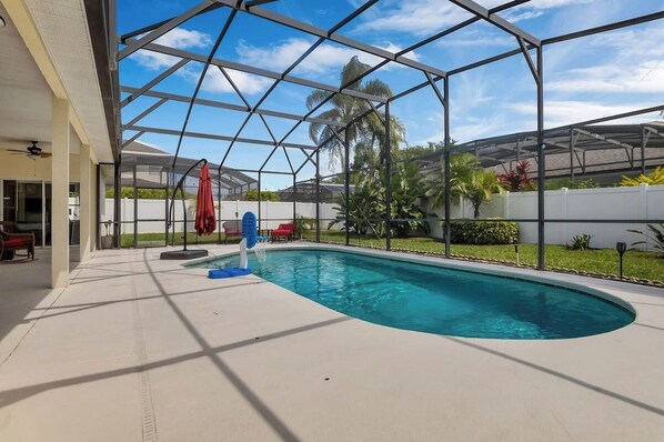 Unwind in this screened-in pool area, featuring comfortable seating and lush greenery—perfect for relaxation and outdoor fun.